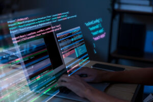 A person works on a laptop displaying multiple screens of code, including React.js components and configuration files. The setup features syntax‑highlighted JavaScript, import statements, and terminal output, creating a focused software‑development workspace.
