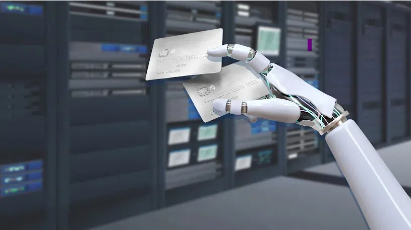 Robot hand holding two credit cards in a data center with server racks in the background.