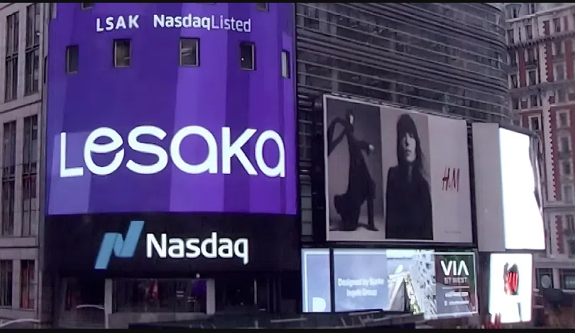 A vibrant Times Square scene featuring tall digital billboards, including a large curved purple display reading “Lesaka” with “LSAK NasdaqListed” above it, positioned above the Nasdaq logo. To the right is an H&M advertisement showing two black‑and‑white fashion portraits. Additional smaller screens display colourful ads and city visuals against the busy urban backdrop.