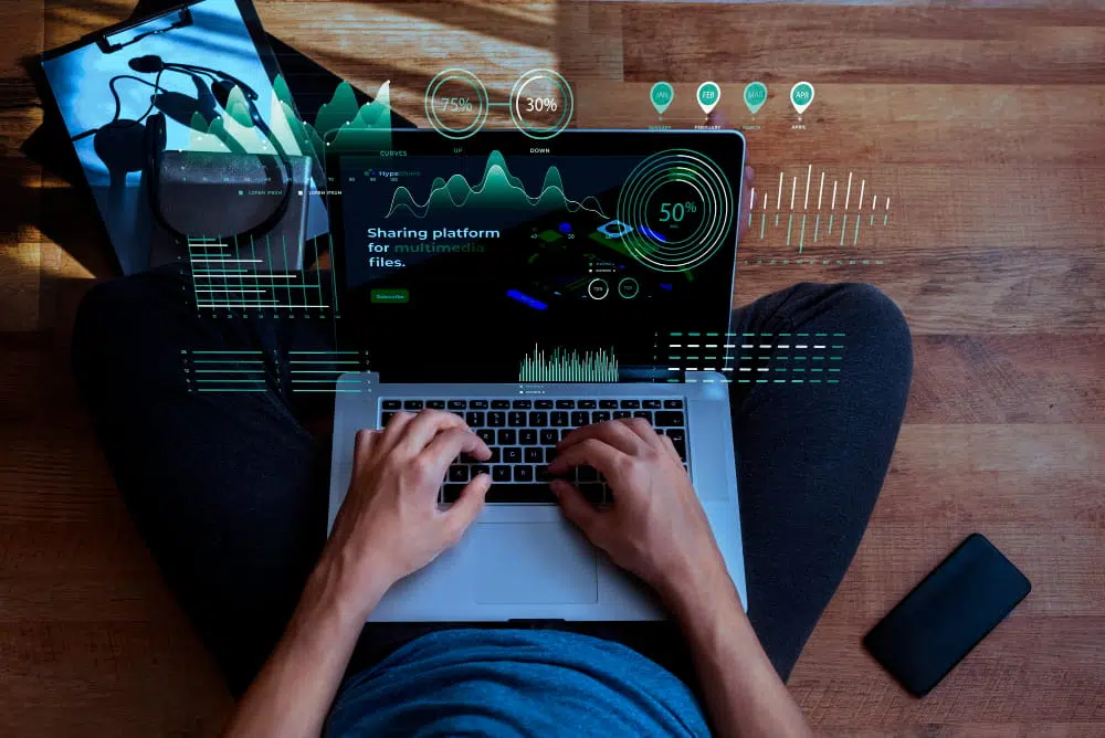 Top-down view of a person typing on a laptop with futuristic data visualizations and charts overlaid on the screen