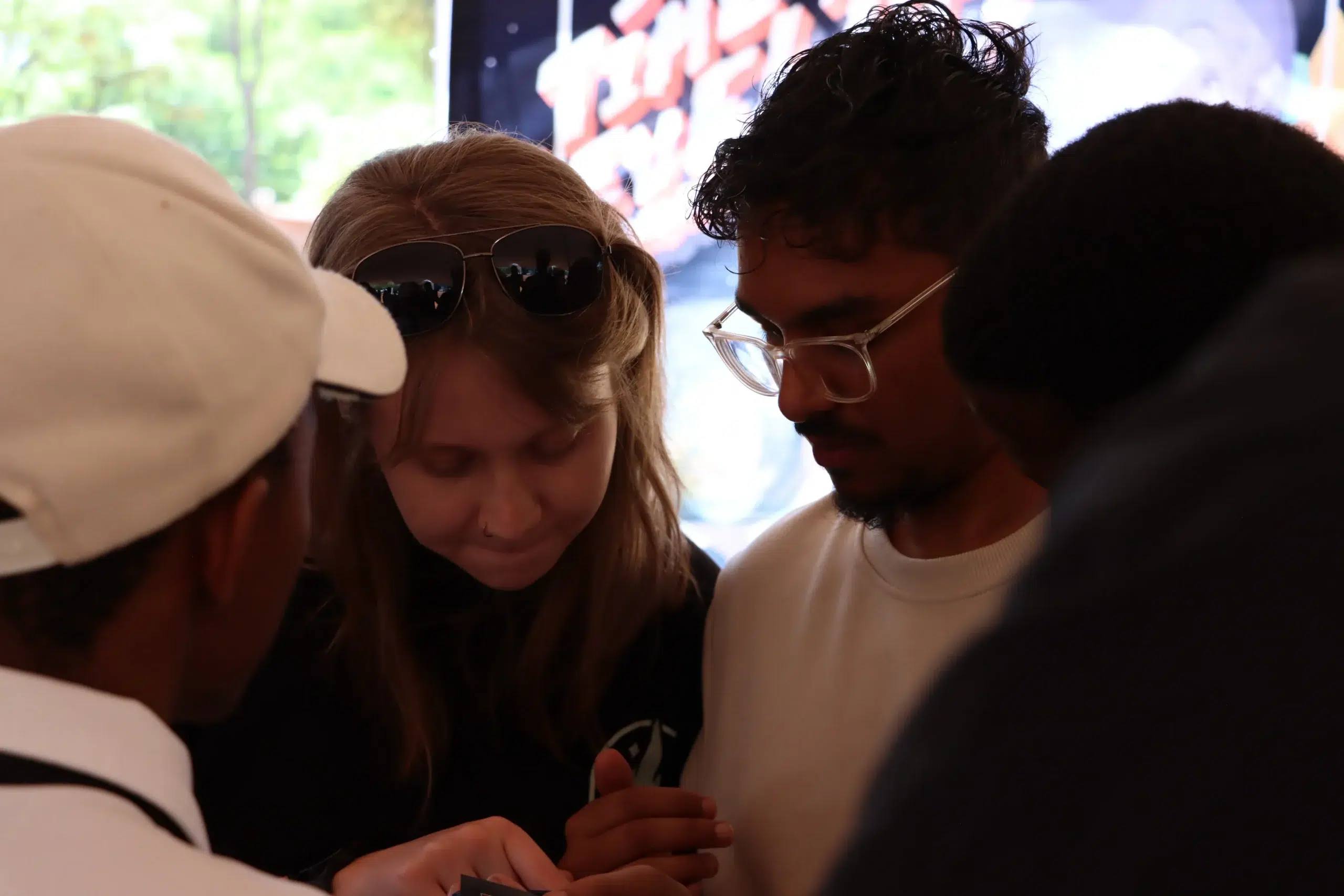 Two young adults lean in close, looking down at something in their hands at a social gathering.