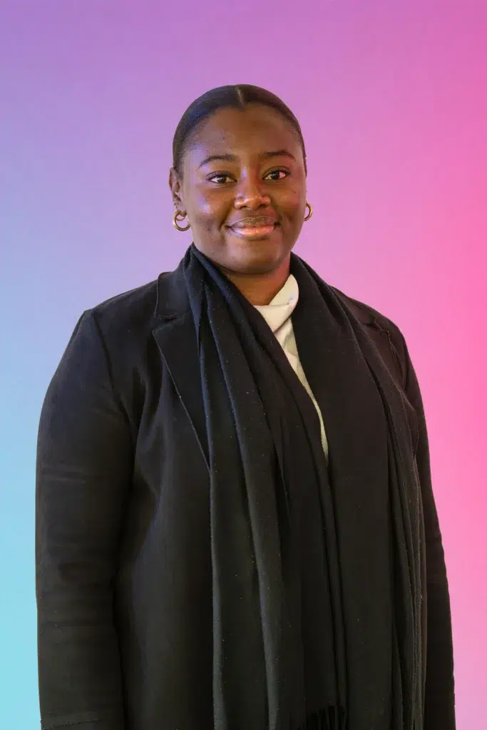 Portrait of a smiling woman in a black coat and scarf against a pink-to-blue gradient background.