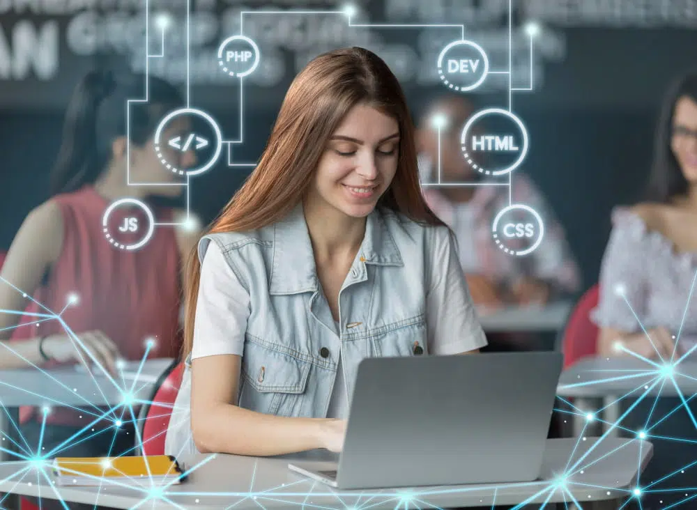 Students sit in a classroom working on laptops, with one student in the foreground focused on coding. Overlaid digital graphics show icons and labels for programming technologies such as PHP, HTML, CSS, JavaScript, and DEV, connected by lines and nodes to represent the relationships between different web development tools.