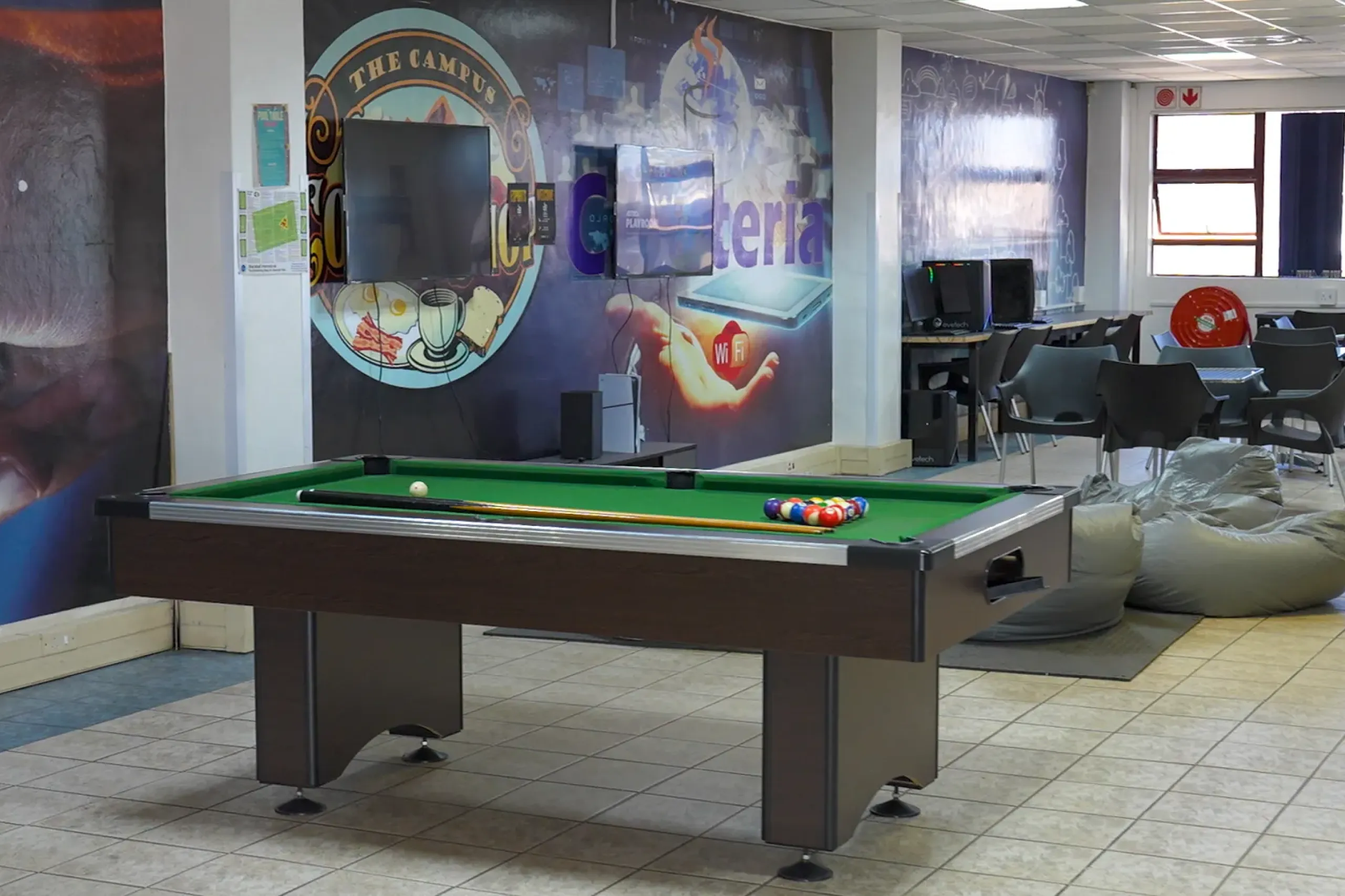 Pool table in a lounge area with chairs, wall mural, and a flat-screen TV on the wall behind it.
