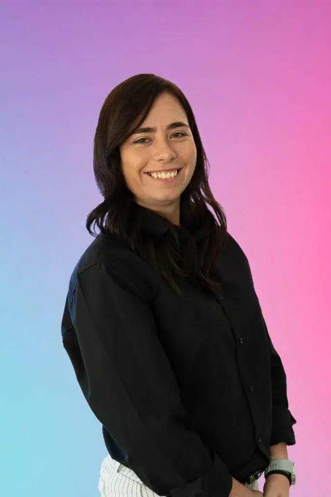 Smiling woman with shoulder-length dark hair wearing a black shirt, against a blue-to-pink gradient background.