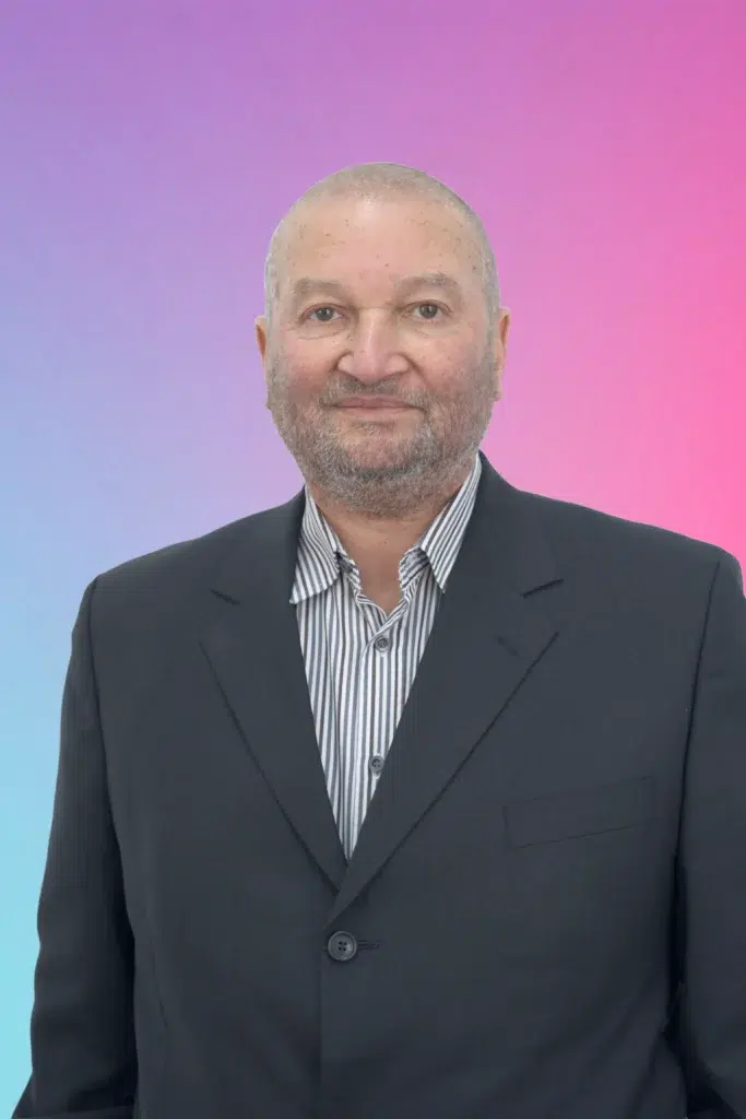 Portrait of a middle-aged man in a dark blazer and striped shirt, smiling against a pink-to-blue gradient background.