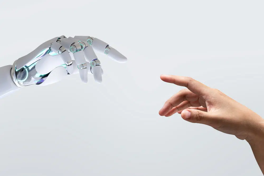 Robotic hand and human hand reaching towards each other against a light grey background, symbolising collaboration between people and artificial intelligence.