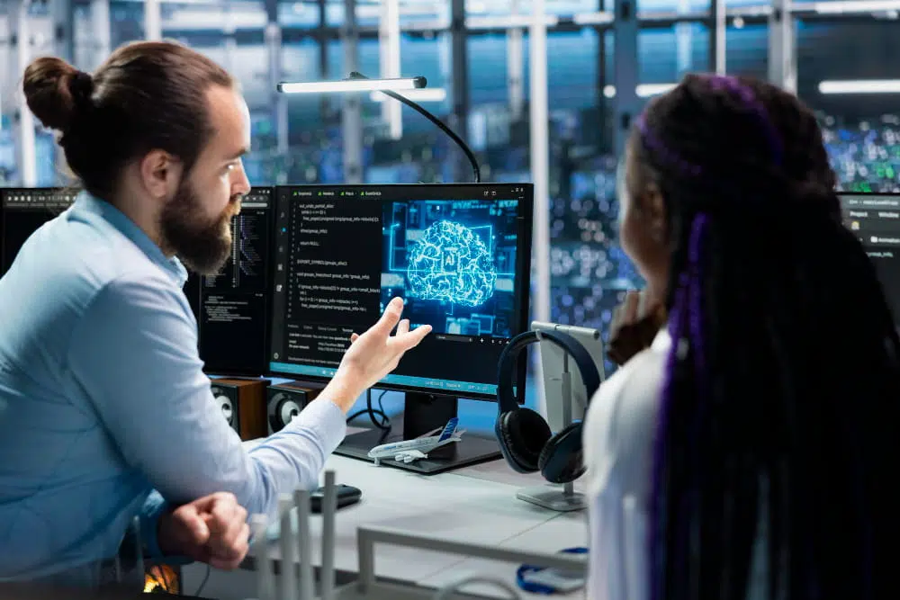 Technology professionals discussing an artificial intelligence project while analysing AI models and code on computer monitors.
