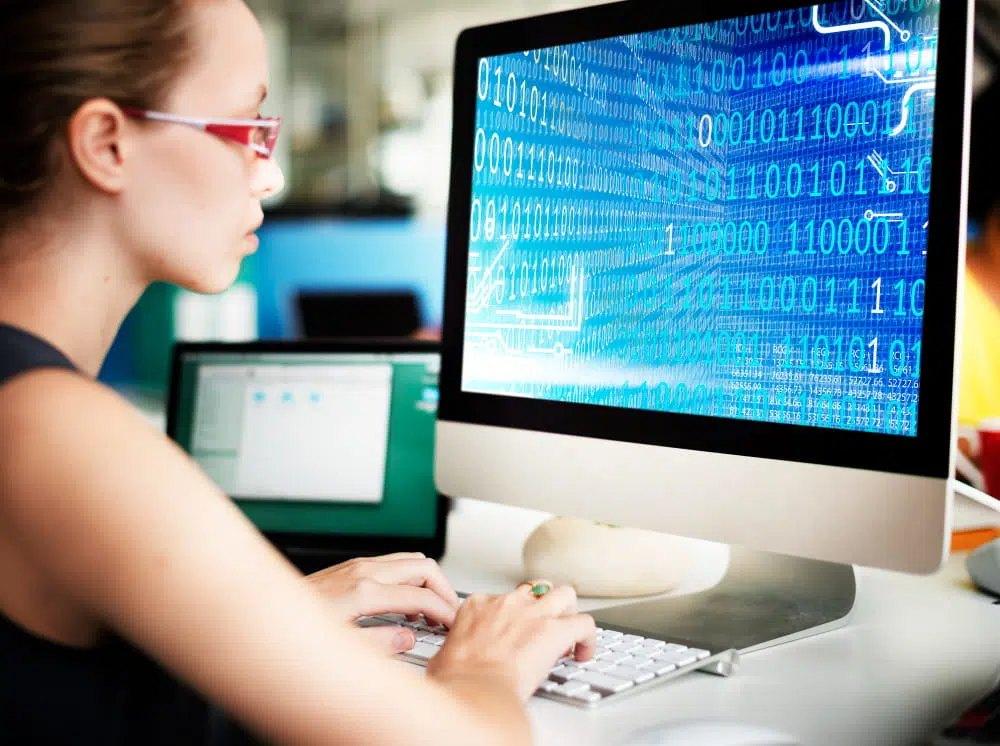 Person coding on a computer with binary data displayed on screen, representing software development, computer science, programming and information technology careers.